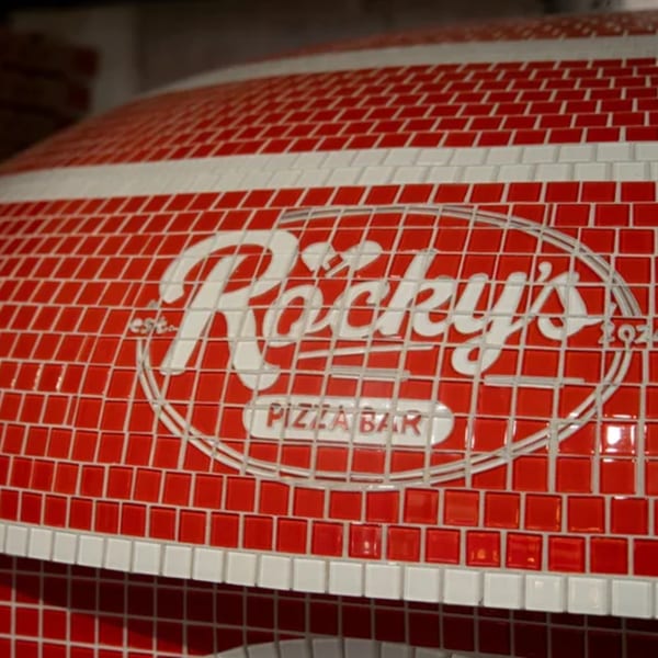 Rocky's Pizza Bar logo in white mosaic tiles on a red tiled pizza oven.