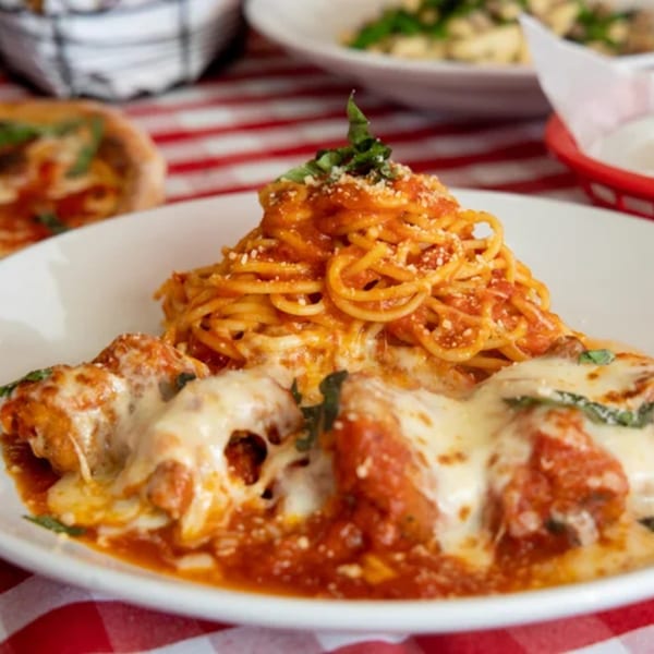 Spaghetti with red sauce and meatballs covered in melted cheese on a white plate.