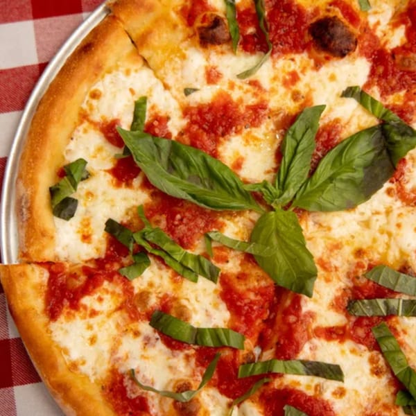 A Rocky's Pizza Bar Margherita pizza with fresh basil leaves on a red and white checkered tablecloth.