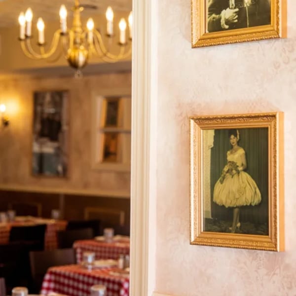 Framed vintage photos on a patterned wall, with a blurred view of a dining room with red checkered tablecloths.